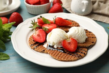 Tasty Dutch waffles (stroopwafels) with ice cream, chocolate sauce, mint and strawberries on light blue wooden table, closeup