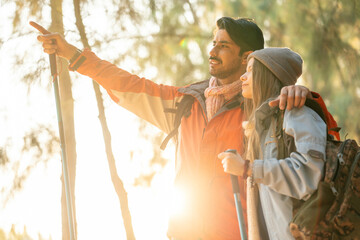 Romantic Couple Hiking in the Forest During Golden Hour. Embracing While Watching Sunset Light Through Trees, Wearing Warm Jackets and Backpacks, Feeling Connected and Adventurous in Nature
