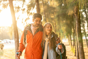 Romantic Couple Hiking in the Forest During Golden Hour. Embracing While Watching Sunset Light Through Trees, Wearing Warm Jackets and Backpacks, Feeling Connected and Adventurous in Nature