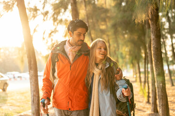 Romantic Couple Hiking in the Forest During Golden Hour. Embracing While Watching Sunset Light Through Trees, Wearing Warm Jackets and Backpacks, Feeling Connected and Adventurous in Nature