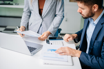 Professional man and woman collaborating on business strategy with laptops in office. Modern teamwork, corporate planning