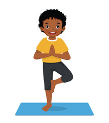Fototapeta premium Little African boy doing yoga pose on a green mat at home 