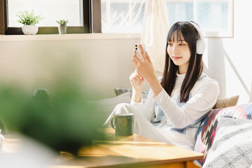 ローソファーに座りスマートフォンで音楽を聴く若い女性
