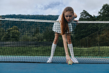 Young athlete retrieving a tennis ball on the court, showcasing determination and focus while...
