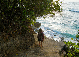 A female tourist with a backpack is descending the stairs to Green Bowl Beach in Bali, Indonesia.