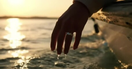 Hand touches water surface from boat at golden sunset hour feeling calm and peaceful moment