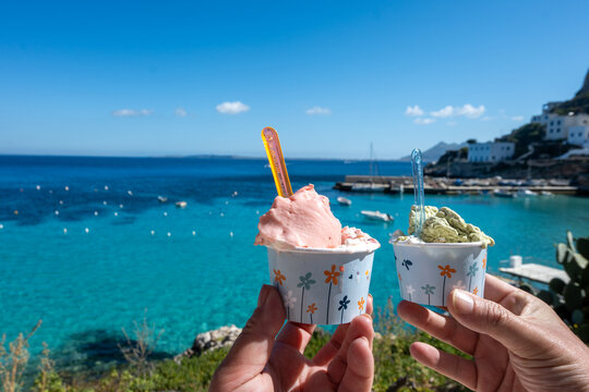 Eating of fresh made ice cream with view on blue bay of Levanza island, Egadi near Sicily, Italy