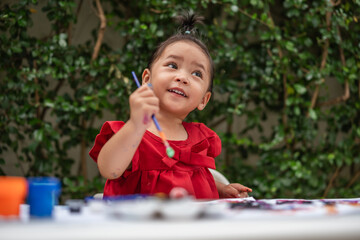 happy toddler girl painting watercolor in paper at backyard.