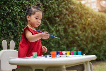 happy toddler girl painting watercolor in paper at backyard.