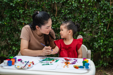 happy mother and toddler girl painting watercolor in paper at backyard.