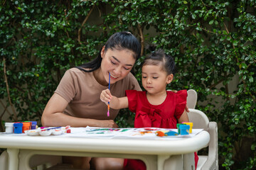 happy mother and toddler girl painting watercolor in paper at backyard.