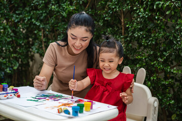 happy mother and toddler girl painting watercolor in paper at backyard.