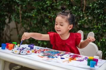 happy toddler girl painting watercolor in paper at backyard.