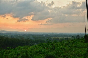 Serene view of a tranquil countryside with vibrant green fields at sunrise. Tranquil atmosphere enhanced by the interplay of colors in the sky, evoking peace and calmness.