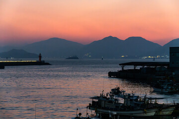 Obraz premium light house, and fishing boats moored at the harbor during sunset