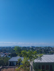 Panoramic view of a small tropical town with corrugated metal roofs, lush green trees, clear blue sky, and distant mountain range