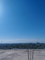 Open construction site with exposed rebars and panoramic view of a tropical town under a clear blue sky and distant mountain range