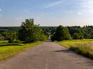 A paved road in the middle of a grassy field with trees on both sides