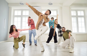 Dancer man and group of young dancing people actively dancing indoors, moving and posing in studio...