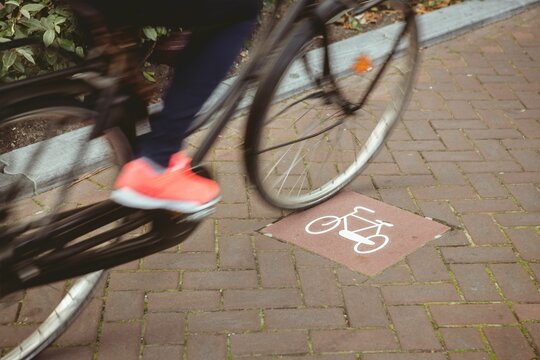 Fototapeta Cyclist front wheel and foot are pedaling on flat design brick-paved lane with white bike marking