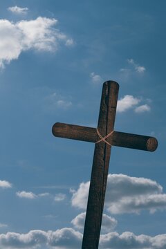 Fototapeta Wooden cross with rope binding is standing against blue sky with white clouds in flat design