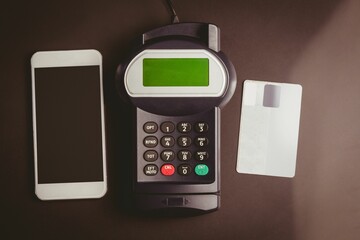 Top-down flat design is showing smartphone terminal white credit card on dark brown matte tabletop