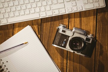 Vintage film camera is resting beside keyboard and notebook with pencil in flat design workspace