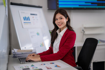 Asian businesswoman working on laptop with charts and graphs in modern office