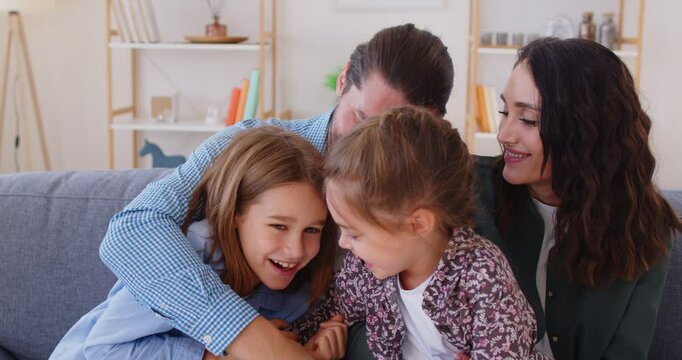 Happy family sitting together on sofa, laughing and hugging. Joyful father, mother and little daughter tickling laughing boy, having fun together and fooling around during family leisure time.