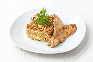Appetizing dish featuring seasoned chicken breast alongside a golden layered casserole garnished