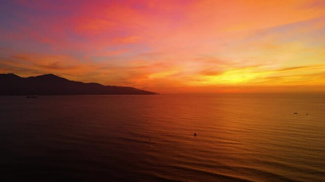 Warm sunset illuminating da nang coastline, golden light painting tranquil waters with mountain silhouettes against dramatic vietnamese seascape
