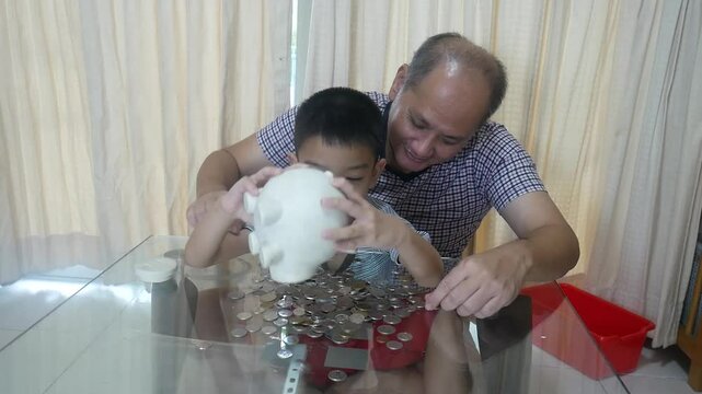 Father and son put coins into a piggy bank together.