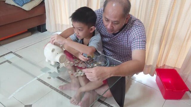 Father and son put coins into a piggy bank together.