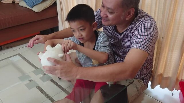 Father and son put coins into a piggy bank together.