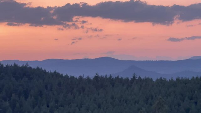Evening twilight over mountains with forested hills and warm sunset colors painting the sky &mdash; peaceful and scenic natural landscape