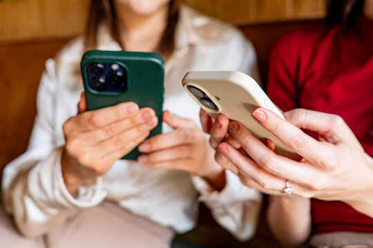 Close-up of two women holding smartphones, browsing internet, using mobile apps, reading news, scrolling social media