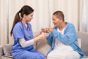 Nurse handing pill cup to senior woman, both engaging in daily care routine in cozy living room,...