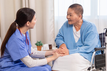 Senior woman in wheelchair discussing health with nurse on sofa, both smiling and sharing emotional...