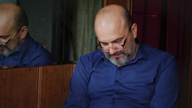 A contemplative and serious mood is captured as a bald man with a beard and glasses looks down with a focused expression, suggesting deep thought, concern, or a moment of quiet reflection