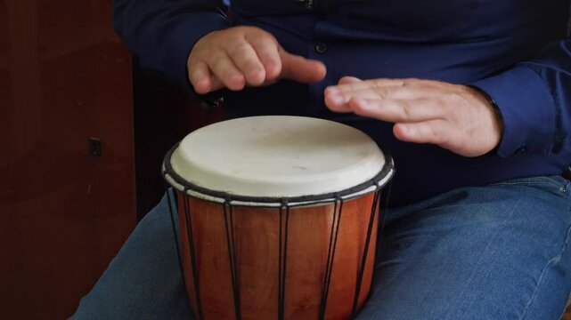 An artistic and rhythmic mood is captured as hands are poised over or actively playing the head of a djembe drum, highlighting the act of creating music