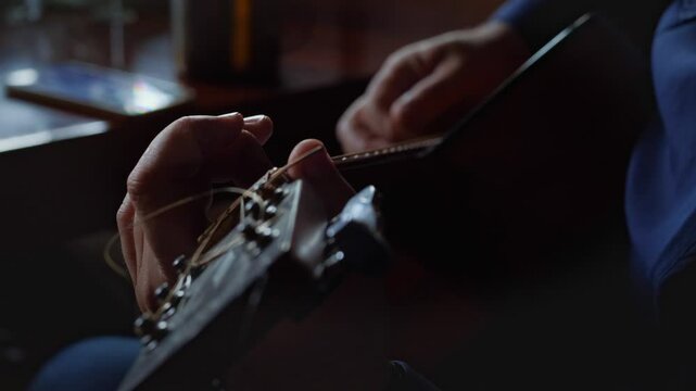 A focused and artistic mood is captured by a close-up of hands expertly pressing and strumming the strings of an acoustic guitar, highlighting the intricate details of playing