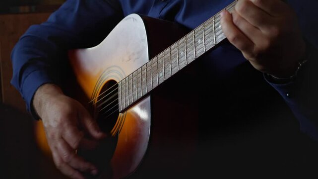 A creative and musical mood is captured by a close-up of hands expertly strumming the strings of an acoustic guitar, highlighting the intricate details of playing and the production of sound