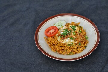 fried noodles with fried egg and sliced ​​cucumber and tomato on a white plate, on the table