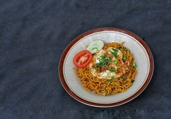 fried noodles with fried egg and sliced ​​cucumber and tomato on a white plate, on the table