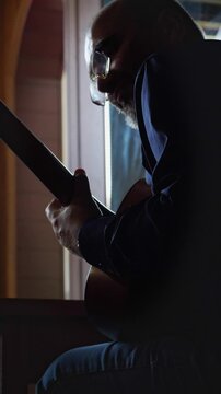 An intimate and dedicated mood is captured as a bald man with a beard intensely plays an acoustic guitar, his gaze fixed on the fretboard. This shot is ideal for depicting musical talent