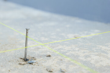 A close-up of a nail driven into rough concrete with intersecting yellow lines, representing detailed construction work for house tiling projects.