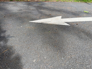 Arrow sign on the asphalt road with shadow on the ground.