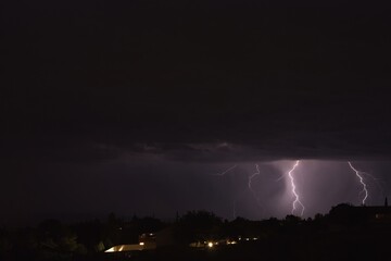 Lightning bolts striking the ground during a storm in Arizona. City lights are in the foreground.