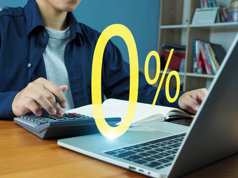 People using calculators and laptops with zero percent symbols representing interest rates or discounts, doing financial calculations in a home office environment.