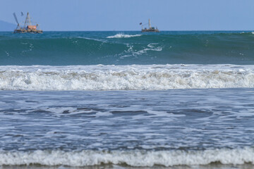 Ocean waves crashing on a sandy beach with clear blue water on a sunny day (Foto Ombak)